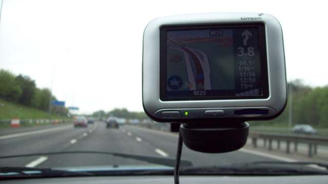A TomTom navigator on a windshield mount above a motorway
